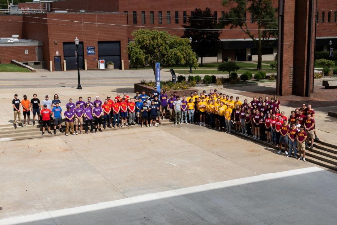 Kettering Greek Life students wearing shirts that represent each fraternity or sorority pose for a group photo outside